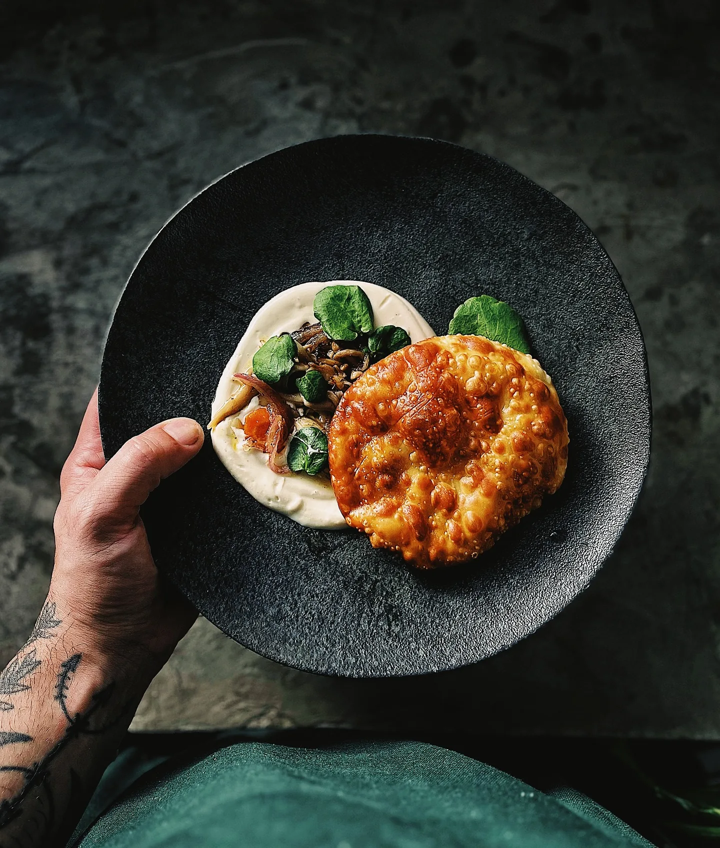 Prato preto com focaccia dourada sobre creme, cogumelos e agrião
